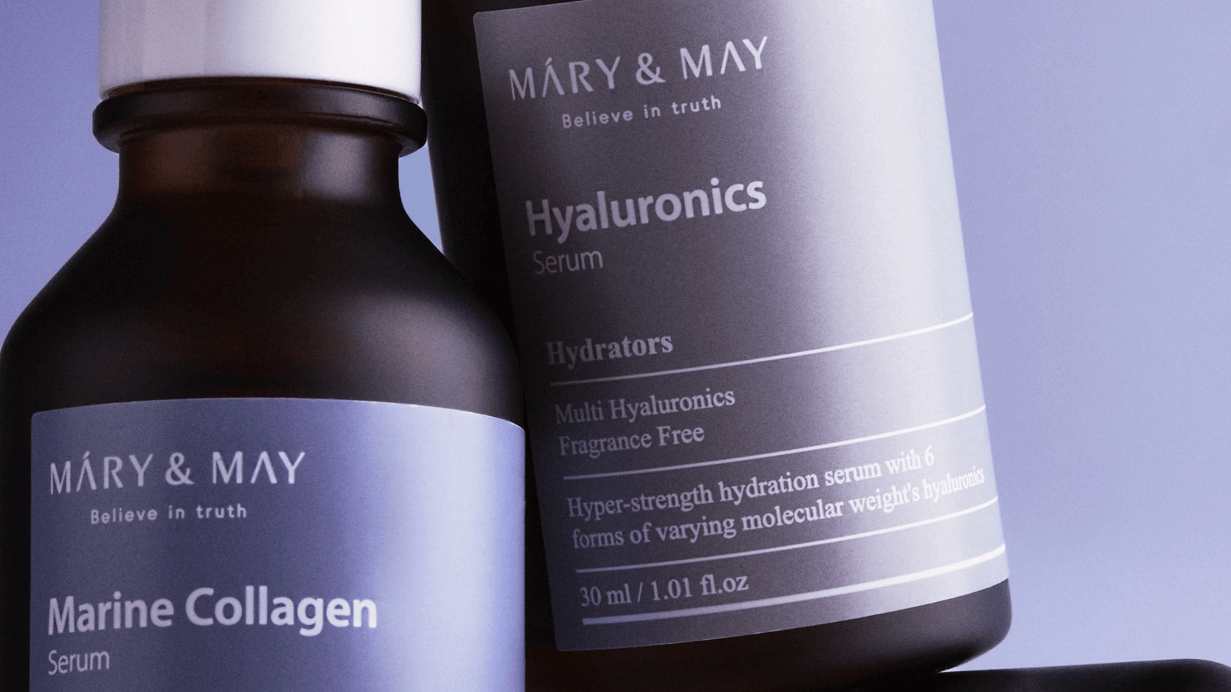 Produktbild av två serum från MARY & MAY: Marine Collagen Serum och Hyaluronics Serum. Båda flaskorna är eleganta med mörka nyanser och silver text som ger information om serumets egenskaper, som fuktgivande och doftfri.