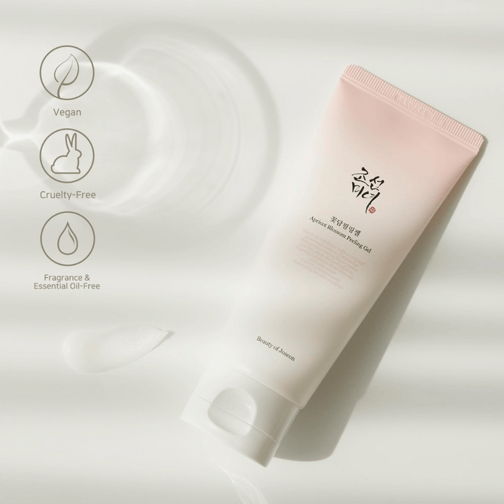 En tub med Apricot Blossom Peeling Gel ligger på en reflekterande yta med ikoner som anger att produkten är vegan, djurvänlig och fri från doft och eteriska oljor.