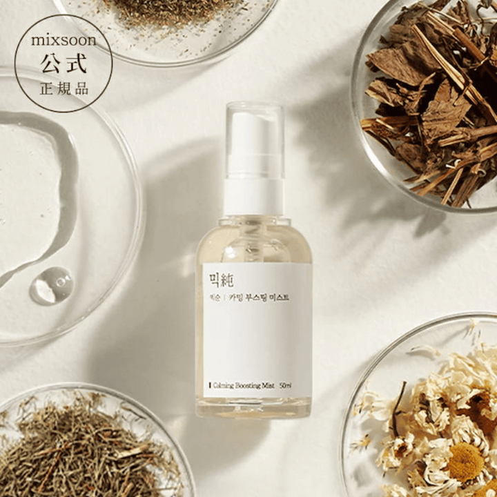 En genomskinlig sprayflaska med etiketten 'Calming Boosting Mist' från Mixsoon, omgiven av torkade örter och blommor på vita skålar mot en beige bakgrund, vilket framhäver produkternas naturliga ingredienser.