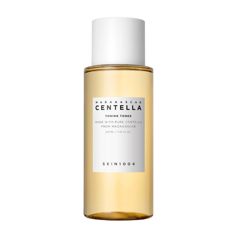 Bilden visar en flaska med hudvårdstoner, märkt "Madagascar Centella Toning Toner" från SKIN1004. Produkten är angiven att innehålla 210 ml eller 7.10 fl.oz och är tillverkad med ren Centella från Madagaskar. Förpackningen är enkel och stilren med en genomskinlig flaska och guldig toner vätska inuti, vilket ger en känsla av lyx och renhet. Varumärkets logotyp SKIN1004 är tydligt synlig i nedre delen av etiketten.